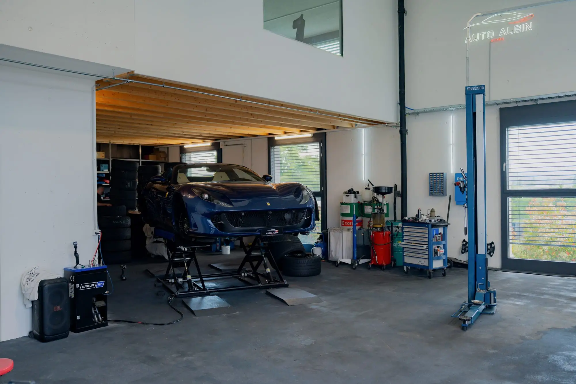 Werkstatthalle von Auto Albin: Sportwagen auf der Hebebühne, Säulenheber, Werkzeugwagen und das beleuchtete Logo an der Wand