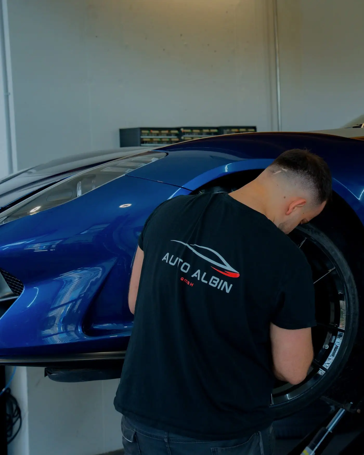 Mechaniker im Auto-Albin-Shirt arbeitet am Rad eines blauen Sportwagens auf der Hebebühne