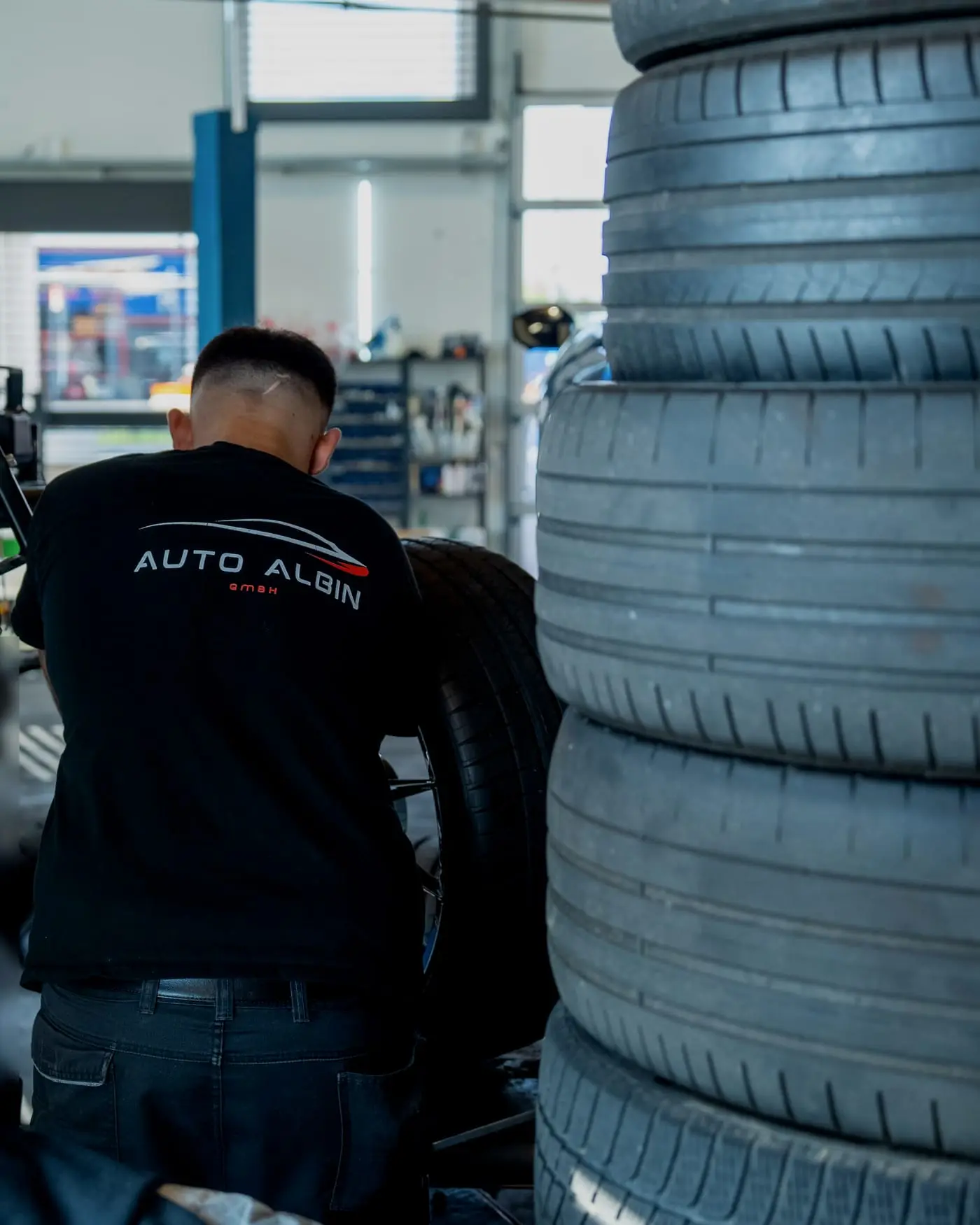 Mechaniker an der Reifenmontiermaschine neben einem Stapel Reifen