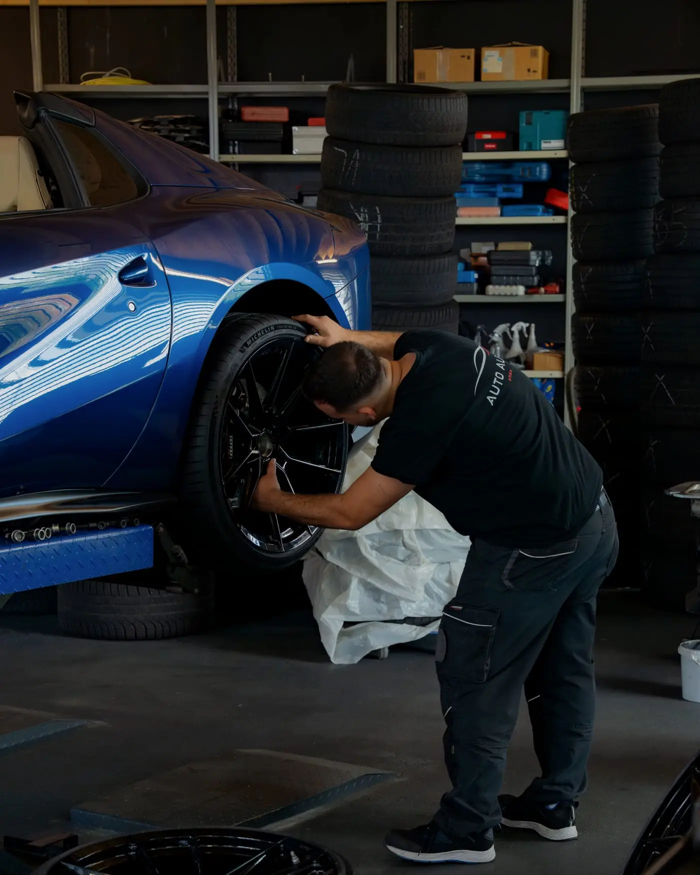 Mechaniker im Auto-Albin-Shirt prüft das Rad eines blauen Sportwagens auf der Hebebühne