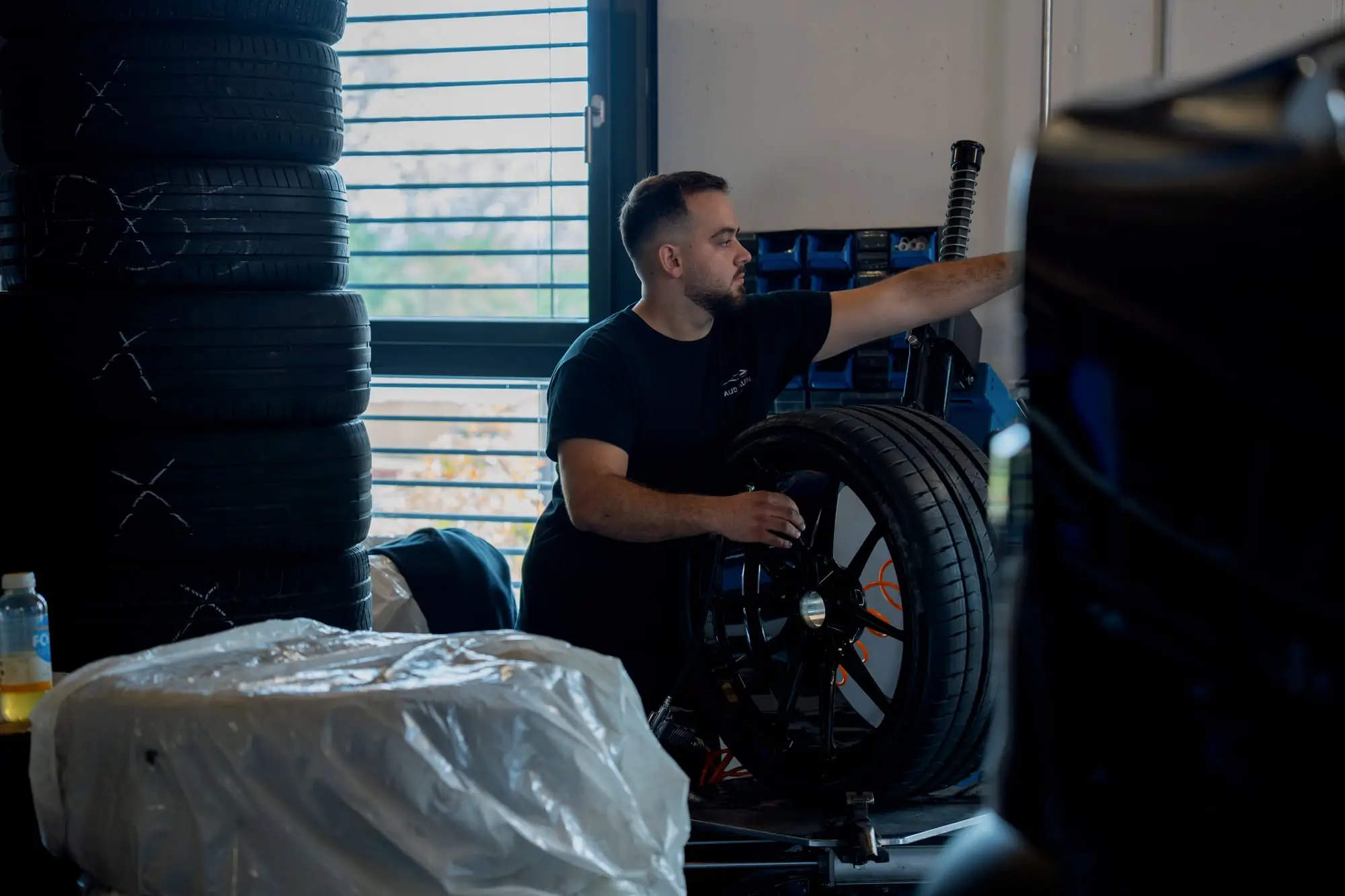 Mechaniker hebt ein Rad mit Sommerreifen neben einem Stapel Reifen am Fenster der Werkstatt