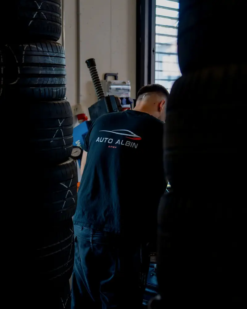Mechaniker im Auto-Albin-Shirt zwischen zwei Reifenstapeln in der Werkstatt in Sins AG